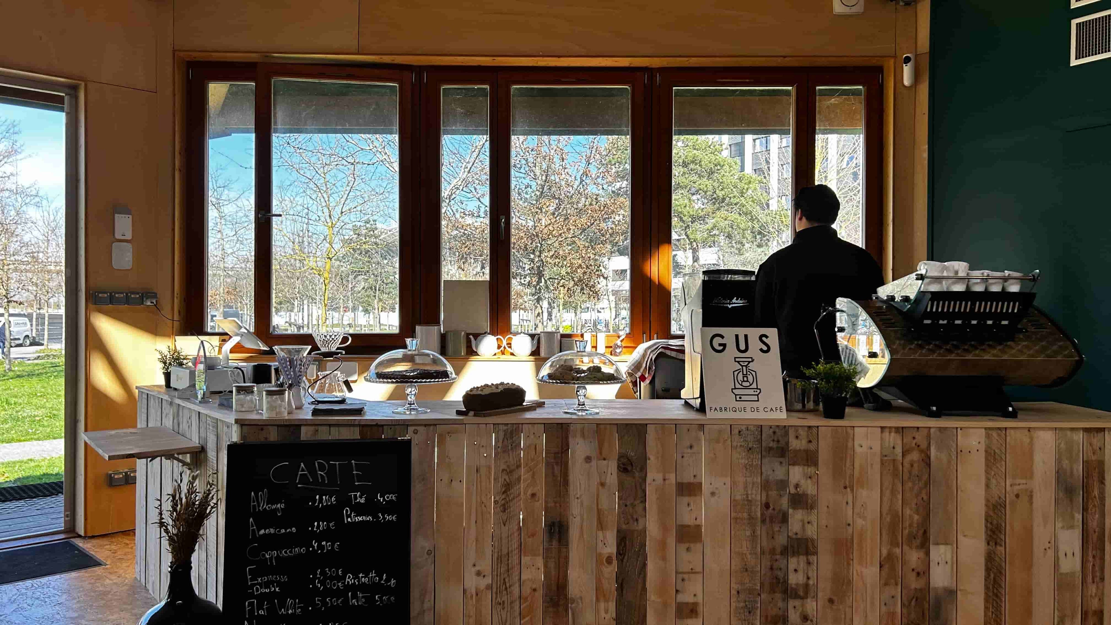 Comptoir ensoleillé du Coffee Shop Café GUS à Palaiseau — barista, machines, pâtisseries et carte des boissons.